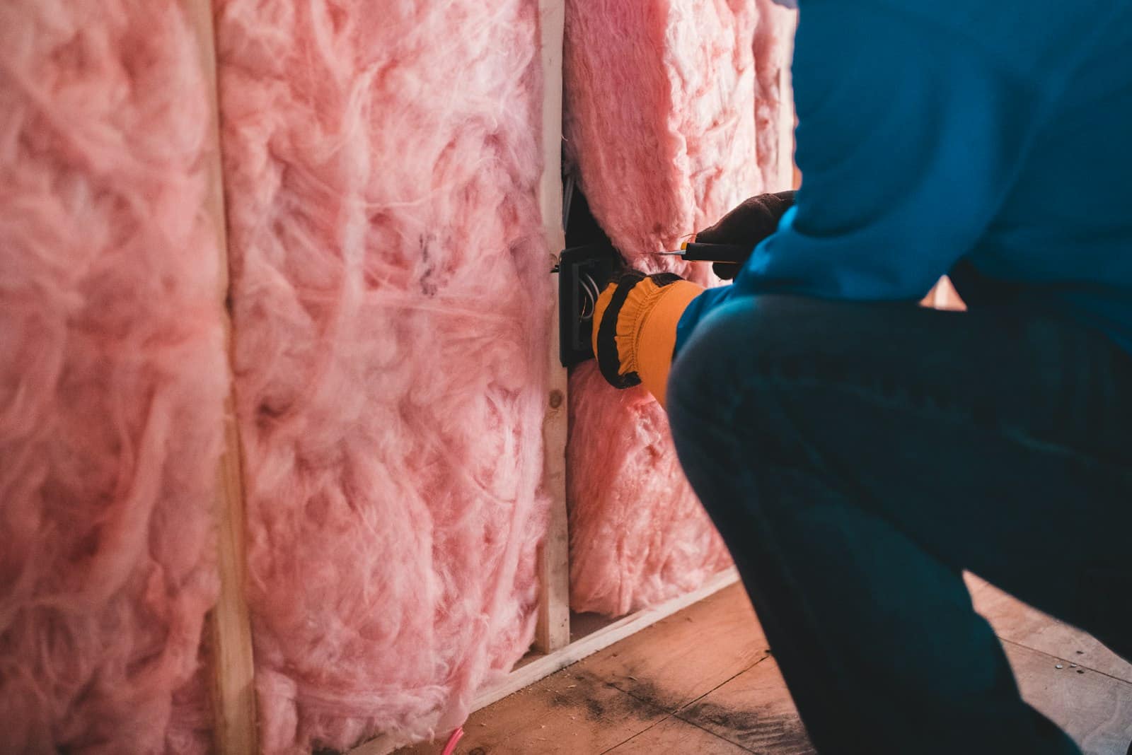A person in a blue shirt installing electrical wiring in pink fibergla